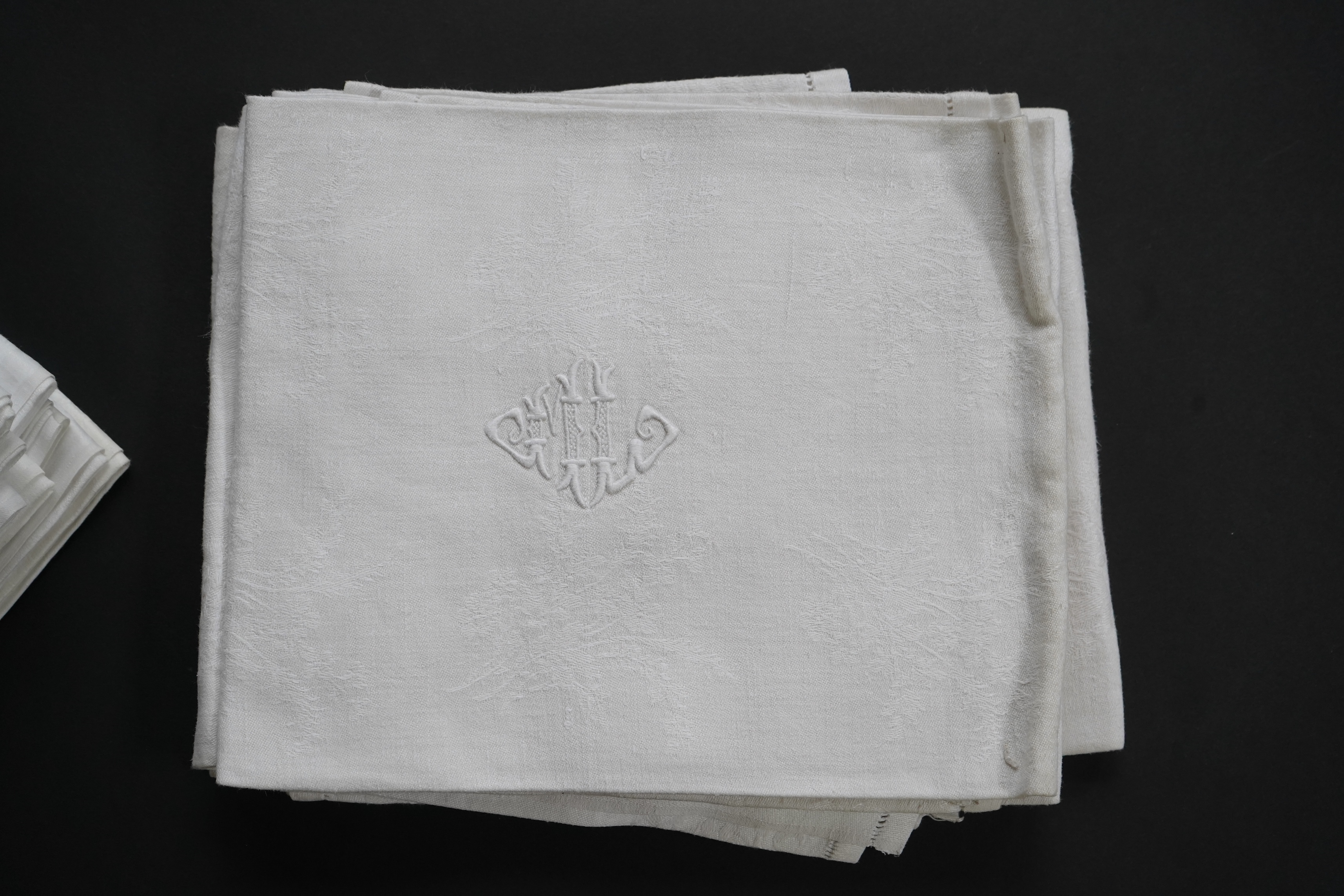 A set of nine red monogrammed 19th century large damask dinner napkins and a similar set of coarser French provincial damask napkins, the large set, decoratively designed with a boating river scene, amongst classical bui